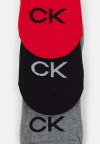 Tre paia di calze nei colori rosso, nero e grigio. Ognuno presenta un grande logo "CK" lavorato a maglia nel tessuto. Materiale morbido e lavorato a maglia.