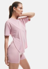 Camiseta atlética de color rosa claro con un corte holgado y dobladillo redondeado, combinada con pantalones cortos ajustados a juego, ambos confeccionados con una tela suave y elástica.