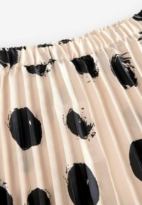 Jupe plissée en tissu doux avec une base crème et de grands motifs circulaires noirs. Taille élastique avec une texture froncée en haut.