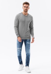 Grijze sweater met een ronde hals, gedragen met versleten blauwe jeans en witte sneakers, wat zorgt voor een casual outfit. Gladde textuur overal.