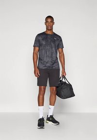 Svart atletisk T-shirt med subtil textur, ihopparad med svarta shorts, svarta sneakers med gröna accenter och en svart gymväska. Vita ankelsockor.