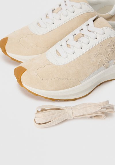 Adidași din suede bej cu accente din piele albă, având o talpă texturată și un model în spirală. Includes un set de șireturi asortate.