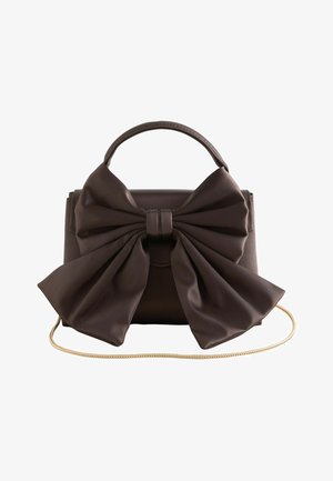 Dunkelbraune Lederhandtasche mit großem, strukturiertem Schleifendetail vorne, obenliegendem Griff und dünnem goldfarbenem Kettenriemen auf weißem Hintergrund.