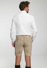 Weißes Langarmshirt mit Knopfdetails, kombiniert mit kurzen Hosen in hellem Beige, aus einem weichen, wildlederähnlichen Material. Einfaches, sauberes Design mit seitlichen Taschen.