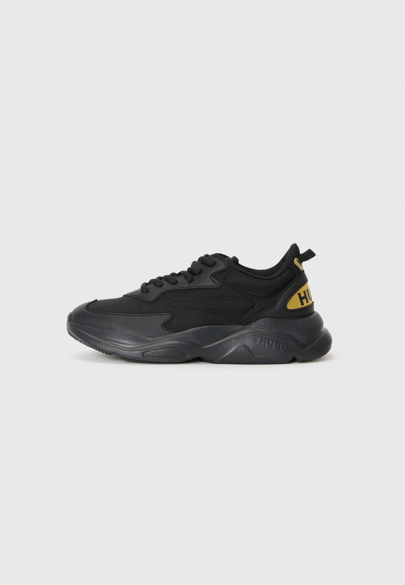 Black sneaker with a textured upper, cushioned sole, and yellow logo. Features lace-up design and a pull tab on the heel for ease of wear.