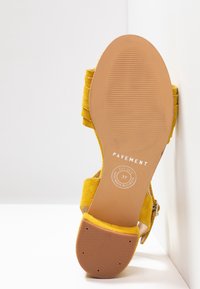 Semelle de sandale en cuir suédé jaune, pointure 37, étiquetée "Pavement" et "Handmade in Europe", positionnée sur un fond d'angle blanc.