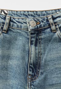 Gros plan de la ceinture d'un jean en denim bleu avec un bouton en métal et des passants de ceinture, montrant des coutures détaillées et la texture du tissu.