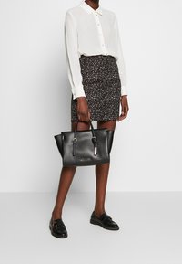 Svart läderhandväska med strukturerad form, silverdetaljer och två handtag. Bärs tillsammans med en vit skjortblus och mönstrad kjol.