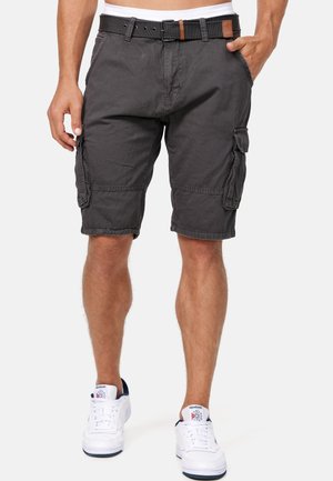 Mand iført mørkegrå cargoshorts med for- og sidelommer, sort bælte, hvide Reebok-sneakers, stående mod en ensfarvet baggrund.