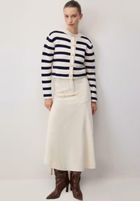 Pleteni kardigan s mornarsko plavim i bijelim prugama, s zlatnim gumbima; uparen s dugom krem suknjom i smešnim čizmama do koljena.