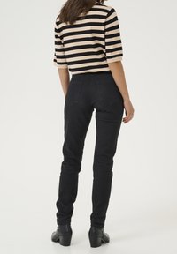 Sorte skinny jeans med høj talje og baglommer, parret med en stribet striktop i beige og sort. Footwear har en kraftig hæl.