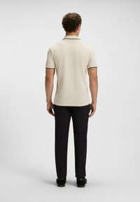 Polo shirt da uomo color crema con colletto a righe nere, maniche corte e design aderente, abbinato a pantaloni e scarpe neri.