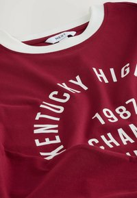 Sweatshirt din bumbac burgundy cu guler rotund și guler alb. Prezintă un text mare imprimat în alb: "Kentucky High 1987 Champion."