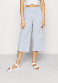 Culotte-broeken in lichtblauw met witte verticale strepen, met een relaxte fit, zijzakken en een elastische tailleband. Gecombineerd met witte sandalen.