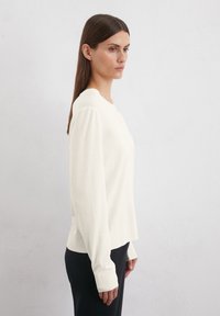 Ljusbeige långärmad topp i mjukt tyg, med rund halsringning och avslappnad passform, med förlängda ärmmuddar och minimal detaljering.