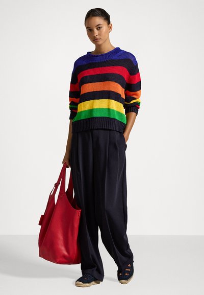Pulover tricotat multicolor cu dungi orizontale în roșu, portocaliu, galben, verde și bleumarin. Asortat cu pantaloni largi bleumarin și o geantă roșie.