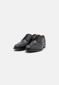 Chaussures de ville en cuir noir avec un design brogue, dotées de détails perforés, d'un bout rond et de lacets plats. Talon en bois classique.