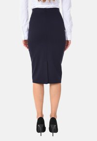 Gonna a matita blu navy con spacco posteriore, realizzata in un tessuto liscio. Indossata con una camicia bianca e scarpe con tacco alto nere.