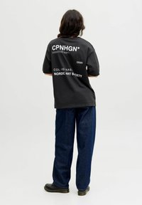 Sort oversized t-shirt med fed hvid tekst på ryggen. Teksten inkluderer "CPNHGN*", "CREATIVE DEP. 2020" og "NORDIC ART SOCIETY."