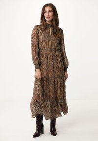 Dlouhé, splývavé šaty v hnědém vzoru s paisley designem. Mají vysoký výstřih, nařasený pas a průhledné rukávy. Kombinují se s tmavými botami.