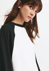 Sort og hvid langærmet raglan T-shirt med rund hals. Blødt stof, kontrasterende ærmer og let tekstur synlig på den hvide del.