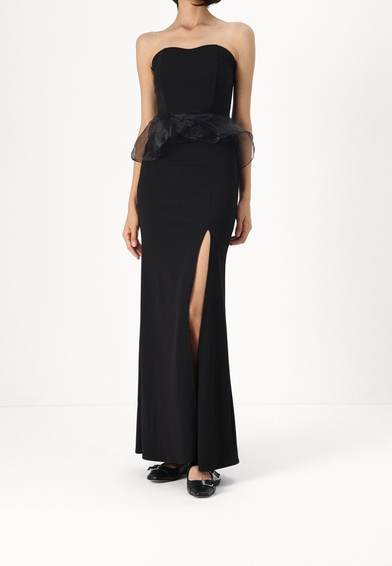 Schwarzes trägerloses Kleid mit herzförmigem Ausschnitt, eng anliegendem Oberteil, transparenter Peplum-Taille, Schlitz bis zum Oberschenkel und bodenlanger Silhouette.