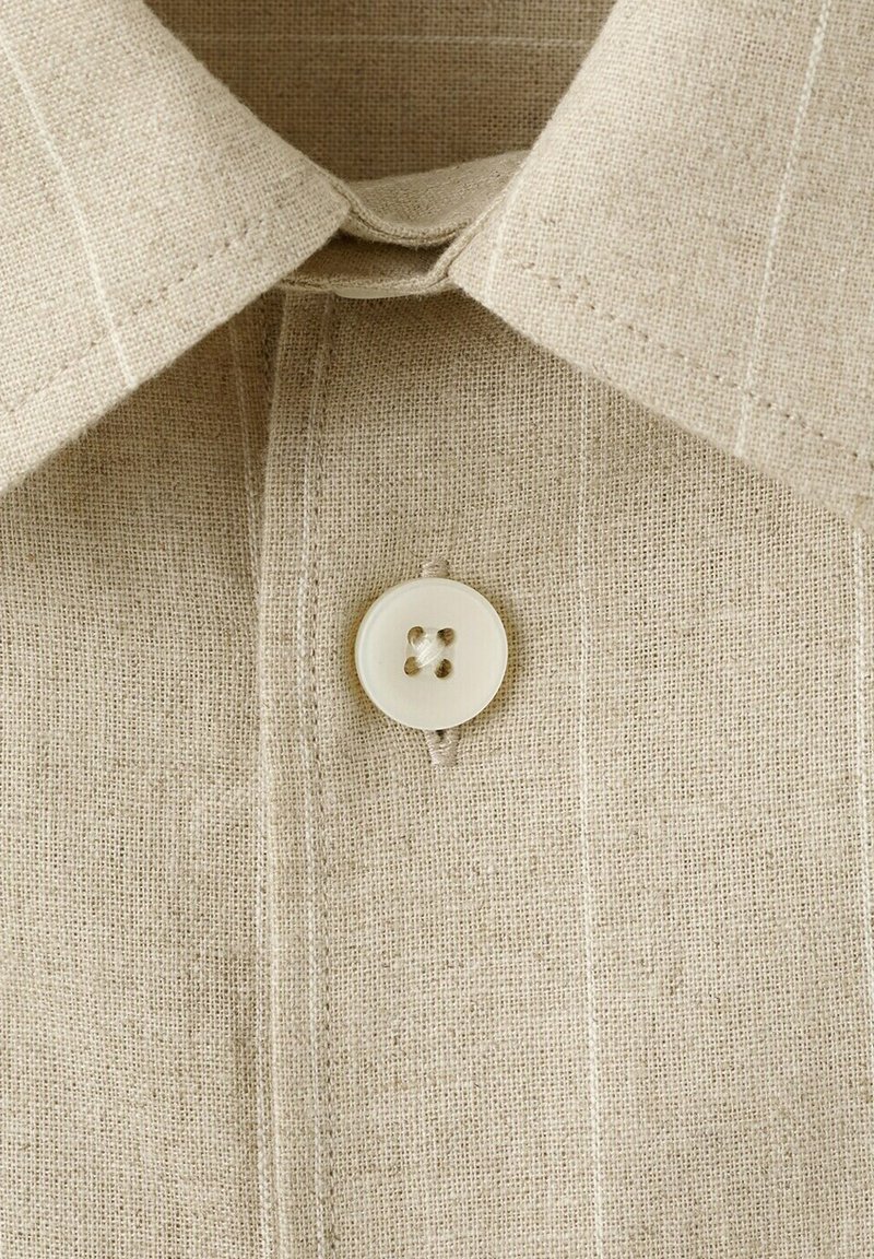 Col de chemise en lin beige avec surpiqûres visibles et un seul bouton rond crème fixé en haut.