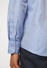 Camicia a fantasia azzurro chiaro con trama a diamante, polsini bottone e design slim fit. Il tessuto ha un aspetto liscio e tessuto.