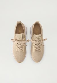 Pair of beige Guess knit sneakers with laces, thick white soles, and logo patches on tongue and lacing area, shown from above.