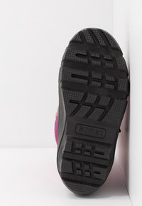 Des chaussures SOREL avec une semelle en caoutchouc noir présentant de profonds motifs de crampons pour une meilleure adhérence, rehaussées par une tige rose. Conception durable et fonctionnelle.