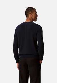 Suéter de punto azul marino con mangas largas, puños y cintura acanalados. Presenta una textura suave y detalles sutiles de costuras en la parte trasera.