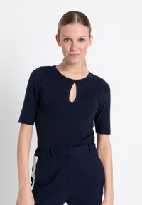 Marineblauw top met korte mouwen en een keyhole-halslijn, gemaakt van een zacht gebreid materiaal. Draagt met high-waisted marineblauwe broek met witte zijaccenten.