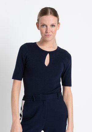 Marineblauw top met korte mouwen en een keyhole-halslijn, gemaakt van een zacht gebreid materiaal. Draagt met high-waisted marineblauwe broek met witte zijaccenten.