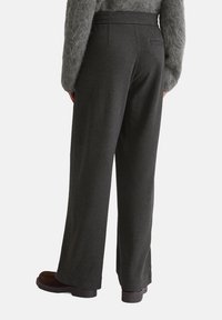 Donkergrijze wijde broek met een gestructureerde afwerking, elastische tailleband en twee achterzakken, gecombineerd met bruine schoenen.