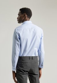 Camisa a rayas azul claro con mangas largas, puños abotonados y cuello estándar, combinada con pantalones oscuros grises que cuentan con bolsillos traseros.