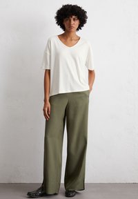 White V-neck t-shirt with short sleeves paired with olive green wide-leg trousers and black flat shoes, creating a relaxed, minimalist look.