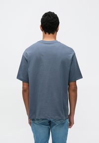 Γκρι βαμβακερό μπλουζάκι με άνετη εφαρμογή, κοντά μανίκια και στρογγυλή λαιμόκοψη. Το ύφασμα έχει λεία υφή και μονόχρωμο χρώμα.