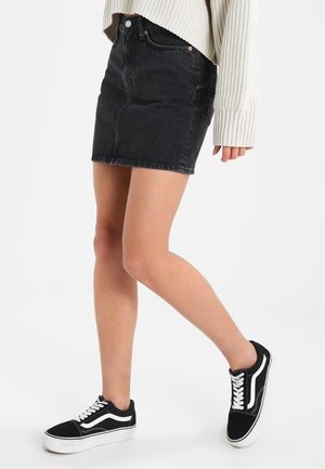 Czarna mini spódnica z dżinsu o dopasowanym fasonie, z przednimi kieszeniami i przeszyciami z dżinsu, zestawiona z czarnymi trampkami Vans z białymi akcentami.