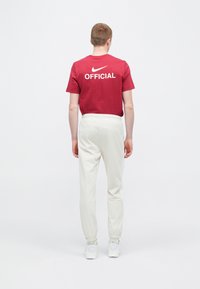 Camiseta roja de algodón con las palabras "OFICIAL" y el logo de Nike en blanco, combinada con pantalones blancos con cintura elástica y puños, llevada con zapatillas blancas.
