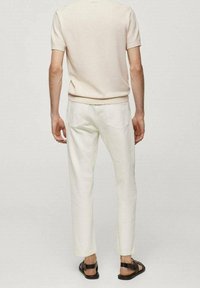 Beżowa, krótkosleeve'owa, dzianinowa bluzka w połączeniu z białymi, zwężanymi spodniami i czarnymi sandałami, prezentująca prosty design i swobodną teksturę.