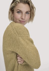Gelber gestrickter Pullover mit weicher Textur, im lässigen Schnitt und mit gerippten Akzenten an den Schultern. Einfaches, minimalistisches Design.