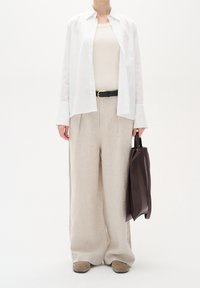 Vit skjorta med knappar, beige linne, ljusbeiga vida byxor, svart bälte, brun väska och beige skor, på en vit bakgrund.