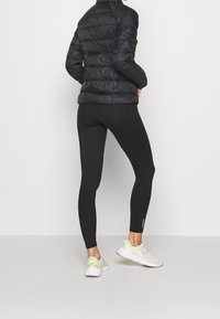 Czarna kurtka puchowa z teksturowanymi panelami, czarne legginsy oraz jasne trampki z neonowożółtymi akcentami i teksturowaną powierzchnią.