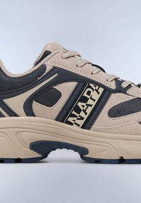 Beige ja tumesinine sneaker, millel on perforeeritud disain, tekstuuritud materjalid ja kuldne kiri. Omab paksu tallatoetust ja kontrastseid aktsente.