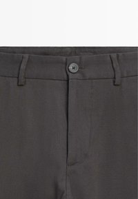 Grå bukser med knaplukning, flad front og sidelommer. Fremstillet af et struktureret stof med tonale syninger.