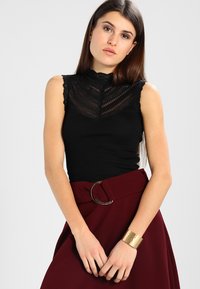 Čierny rebrovaný top bez rukávov s čipkovaným detailom pri krku, skombinovaný s burgundskou sukňou s vysokým pásom a okrúhlou prackou.