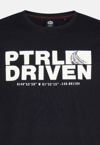 Černé bavlněné tričko s výrazným bílým nápisem "PTRI DRIVEN" a grafickým motivem stopy pneumatiky. Velikost: L. Obsahuje geografické souřadnice v malém písmu.