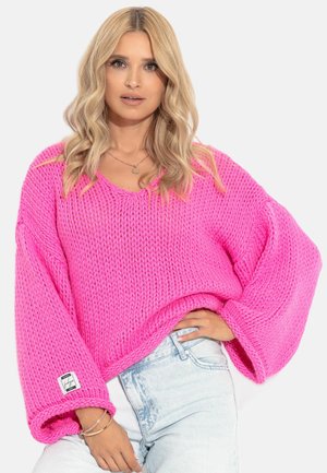 Jasnoróżowy, oversize'owy sweter dzianinowy z szerokimi rękawami i dekoltem w kształcie V. Posiada teksturowany wzór oraz małą metkę z logo na dole.