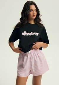 Czarny t-shirt z grafika "Sportcore" w jasnoróżowym kolorze, w zestawie z różowo-białymi szortami w kratkę o elastycznej talii.