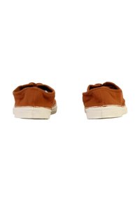 Par de zapatos de lona marrones desgastados tipo slip-on con suelas de goma blanca, vistos desde atrás sobre un fondo blanco.